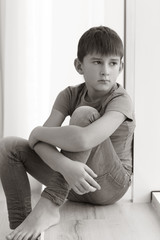 Fototapeta premium Sad little boy sitting on windowsill