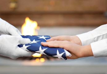 Hands holding folded American flag on Eternal flame background