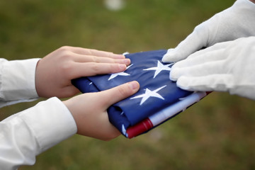 Hands holding folded American flag on green grass background