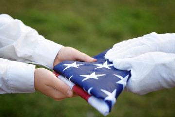 Hands holding folded American flag on green grass background