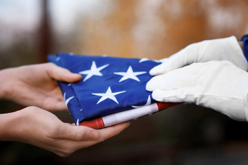 Hands holding folded American flag on blurred background - Powered by Adobe
