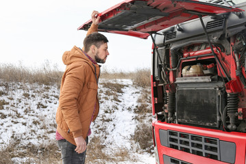 Handsome driver near truck with open hood outdoors