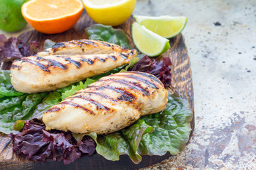 Grilled chicken breast in citrus marinade on salad leaves and wooden cutting board, horizontal, copy space