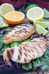 Grilled chicken breast in citrus marinade on salad leaves and wooden cutting board, vertical