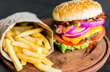 Burger and french fries on a wooden table against black background. Selective focus