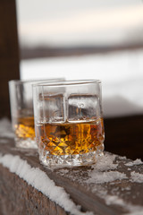 Two whiskey glasses in the snow on a winter background.