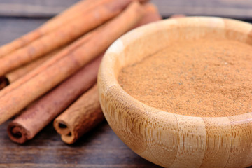 Bowl with cinnamon powder and sticks on table