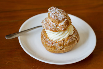 Cream puffs filled vanilla custard and dusted with icing on a rack
