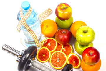 Concept of healthy active lifestyle. Heap of green and red apples and red oranges. Bottle of pure water with flexible ruler. Fitness dumbbell in foreground. Sliced red orange.