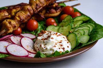 Chicken kebab with vegetables on a clay plate