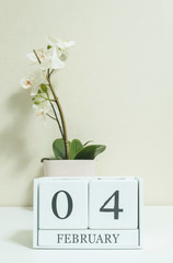 Closeup white wooden calendar with black 4 february word with white orchid flower on white wood desk and cream color wallpaper in room textured background in selective focus at the calendar