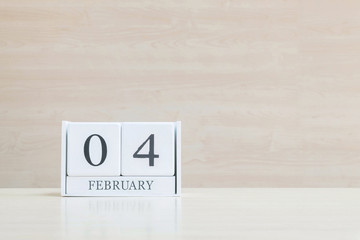 Closeup surface white wooden calendar with black 4 february word on blurred brown wood desk and wood wall textured background with copy space in selective focus at the calendar