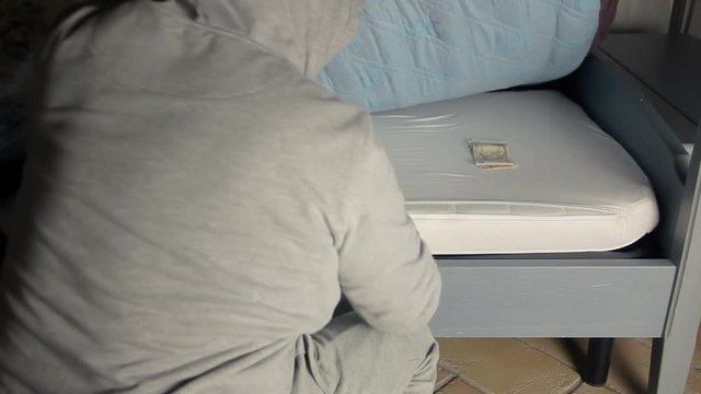A burglar (criminal, thief) stealing money kepy under the mattress. Front shot.
