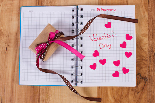 Valentines Day written in notebook, wrapped gift and hearts, decoration for Valentines