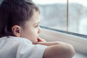 sad little boy sitting near the window