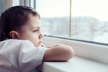 sad little boy sitting near the window