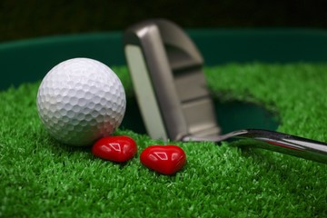 Naklejka premium Golf ball and putter with heart are on green grass