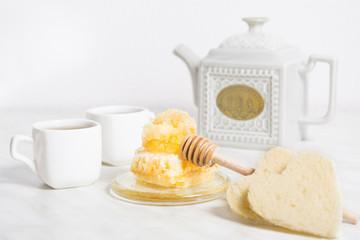 Honey with honeycomb and tea with two pieces of bread and teapot on the background