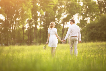 Happy couple - pregnant woman and her husband go on a picnic  the grass.