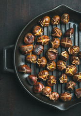 Roasted chestnuts in cast iron grilling pan over dark wooden background, top view, vertical composition
