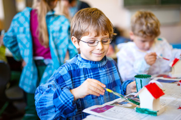 Little school kid boy with glasses coloring bird house with watercolors