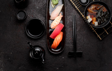 Sushi set on a black plate and miso soup over dark concrete background