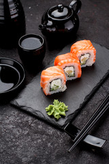 Salmon sushi roll on a stone plate with chopsticks over concrete background.