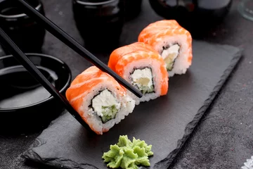 Store enrouleur Bar à sushi Rouleau de sushi au saumon sur une plaque de pierre avec des baguettes sur fond de béton.