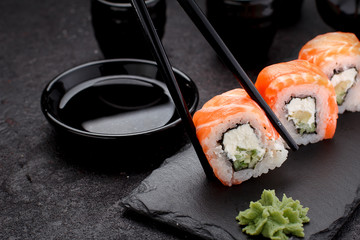 Salmon sushi roll on a stone plate with chopsticks over concrete background.