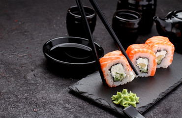 Salmon sushi roll on a stone plate with chopsticks over concrete background.