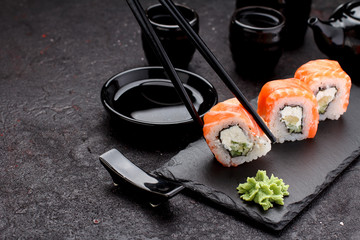Salmon sushi roll on a stone plate with chopsticks over concrete background.