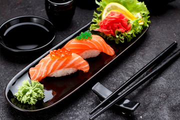 Japanese cuisine. Salmon sushi nigiri on a black plate with chopsticks.