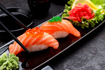 Japanese cuisine. Salmon sushi nigiri on a black plate with chopsticks.