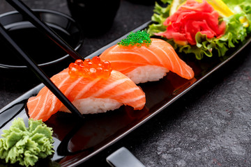 Japanese cuisine. Salmon sushi nigiri on a black plate with chopsticks.