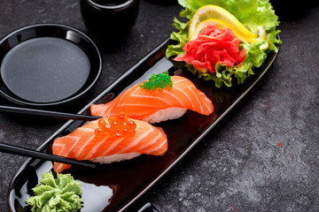 Japanese cuisine. Salmon sushi nigiri on a black plate with chopsticks.