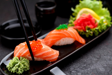 Japanese cuisine. Salmon sushi nigiri on a black plate with chopsticks.