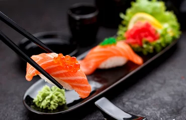 Fotobehang Japanese cuisine. Salmon sushi nigiri on a black plate with chopsticks. © z10e