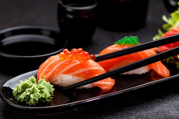 Japanese cuisine. Salmon sushi nigiri on a black plate with chopsticks.