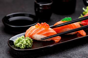 Japanese cuisine. Salmon sushi nigiri on a black plate with chopsticks.