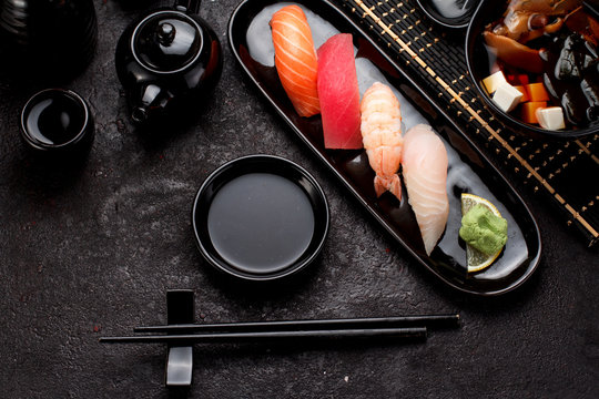 Sushi set on a black plate and miso soup over dark concrete background