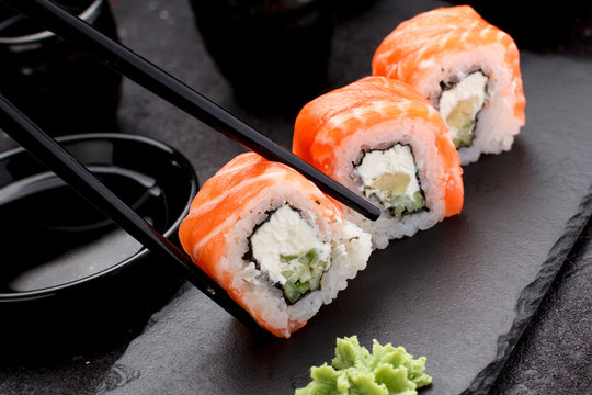 Salmon sushi roll on a stone plate with chopsticks over concrete background.