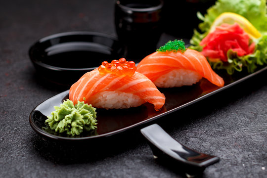 Salmon sushi with soy sauce on a black plate and dark concrete background.