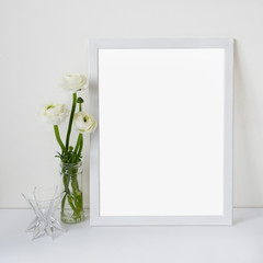 White wooden frame with place for text with ranunculus bouquet in glass vase on a background of a white wall and table. Light romantic style concept, minimalism design