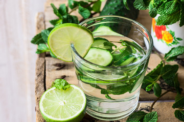 Close up of glass with detox cucumber water with fresh mint and lime on barn wood box, ingredients, spring or summer, outdoors, top angle view
