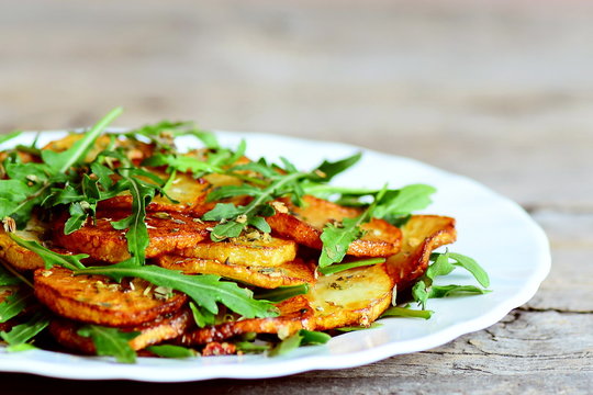 Roasted potatoes with arugula. Combine fresh arugula mixture and hot potatoes on a white plate. Delicious and healthy recipe. Closeup