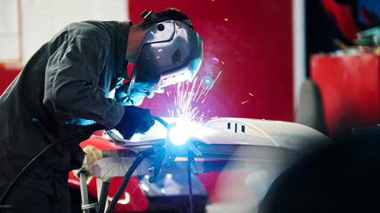 Welding industrial: worker in helmet repair detail in car auto service - blue sparklers