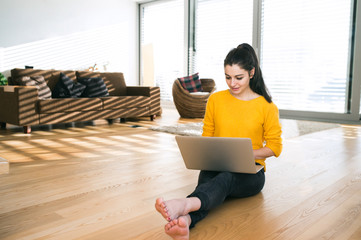 Woman at home sitting on the floor, working on laptop, writing