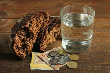 Glass of water, black bread and money on a wooden background. The concept of poverty.