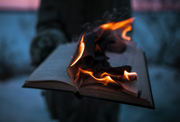 A girl holding a book burning in nature in winter at sunset