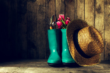 Gardening tools with blue rubber boots, straw hat, spring flower